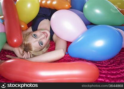 Portrait of teenage girl (16-17) lying on bed under pile of balloons