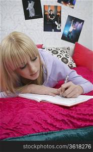 Portrait of teenage girl (16-17) lying on bed, writing diary