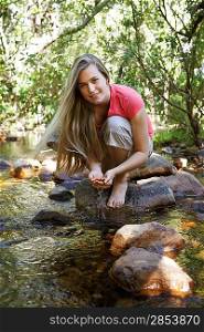 Portrait of teenage girl (16-17 years) squatting on stone by stream in forest smiling