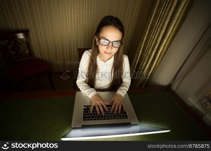 Portrait of teenage girl sitting in dark room with laptop