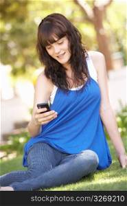 Portrait Of Teenage Girl Sitting In Park Using Mobile Phone