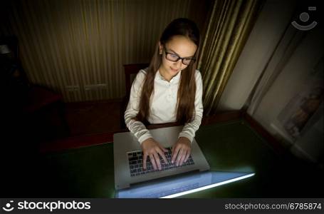 Portrait of teenage schoolgirl working with laptop at late evening