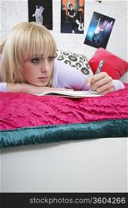 Portrait of teenager (16-17) lying on bed, writing diary