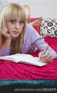 Portrait of teenager (16-17) lying on bed, writing diary