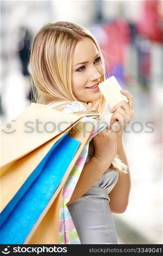 Portrait of the attractive thoughtful blonde with bags and a credit card in shop