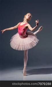 Portrait of the ballerina in ballet pose on a grey background. Ballerina is wearing pink tutu and pointe shoes. Portrait of the ballerina in ballet pose