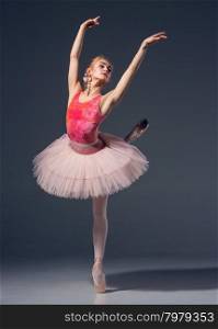 Portrait of the ballerina in ballet pose on a grey background. Ballerina is wearing pink tutu and pointe shoes. Portrait of the ballerina in ballet pose