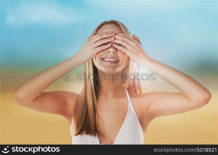 Portrait of the beautiful girl on the beach hiding her eyes with hands