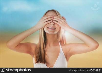 Portrait of the beautiful girl on the beach hiding her eyes with hands