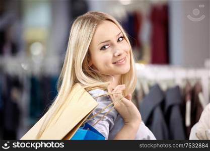 Portrait of the beautiful young blonde with bags in clothes shop