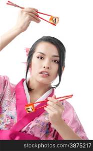 Portrait of the Beautiful Young Japanese Woman Eating Sushi with Two Pairs of Chopsticks, Wearing a Traditional Kimono Dress at the white background
