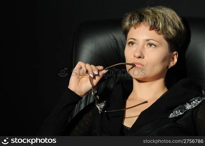 Portrait of the business woman in a leather armchair. A studio photo on a black background