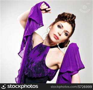Portrait of the fashion woman in violet dress with stylish hairstyle poses at studio