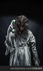 Portrait of the horror zombie girl calling by telephone. Scary. Horror zombie girl calling by phone