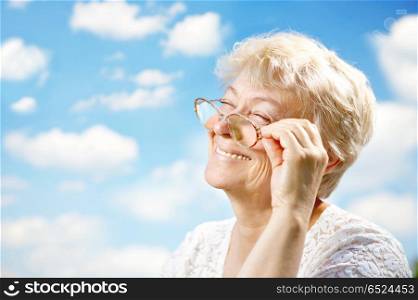 Portrait of the laughing elderly woman with glasses against the sky. Rest