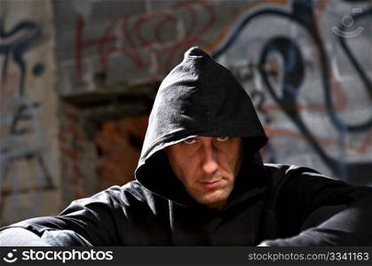 Portrait of the man in a hood against an urbanistic wall