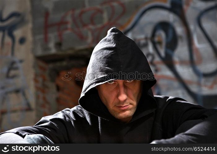 Portrait of the man in a hood against an urbanistic wall. Stranger