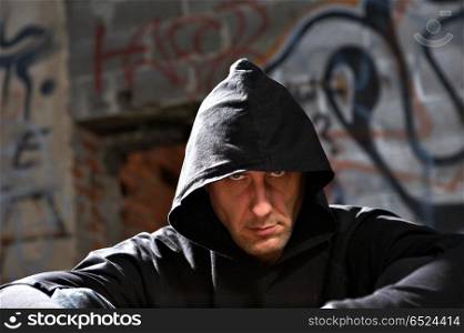 Portrait of the man in a hood against an urbanistic wall. Stranger