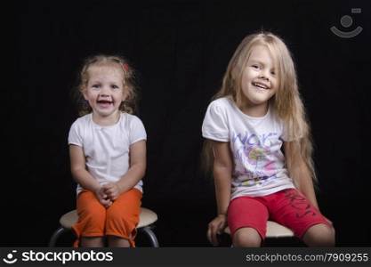 Portrait of the sisters - two little girls on the chairs. Girls fun smiling and looking in the frame.