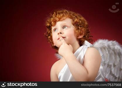 Portrait of the small thoughtful boy with wings behind the back on a red background