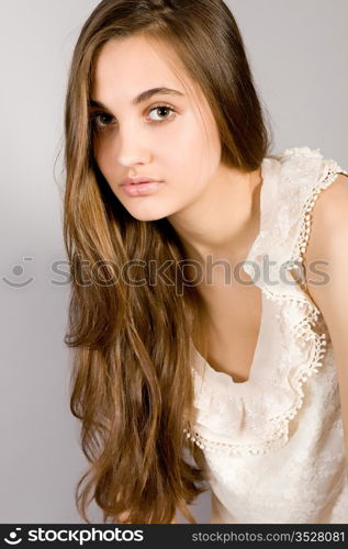 Portrait of the young long-haired girl in an elegant dress on a gray background