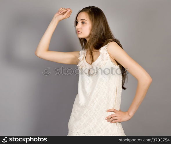 Portrait of the young long-haired girl in an elegant dress on a gray background