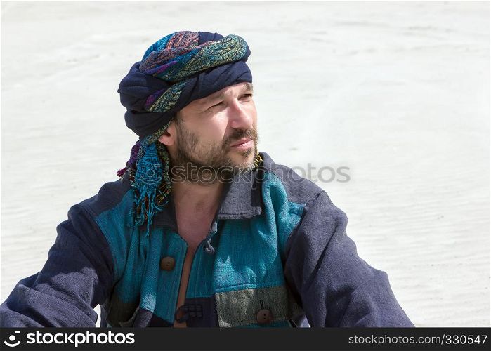 Portrait of thoughtful mature bearded man in his turban with on a background of white sandy desert.. Portrait of a man in his turban against the backdrop of the dese