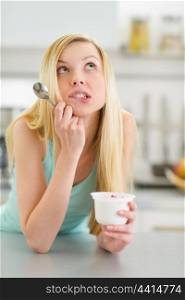 Portrait of thoughtful teenager girl with yogurt in kitchen