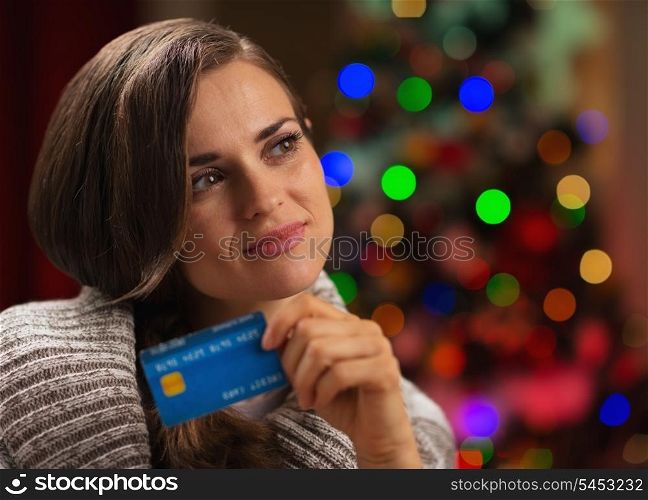 Portrait of thoughtful woman with credit card in front of Christmas lights
