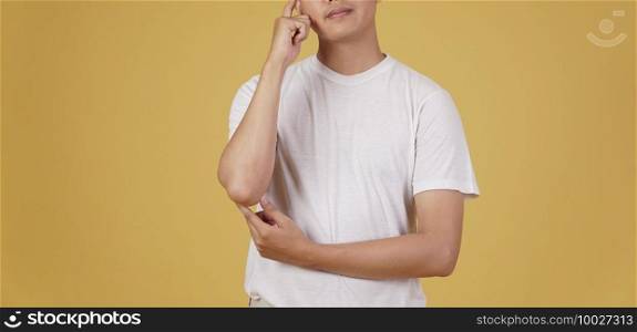 portrait of thoughtful young asian man dressed casually thinking doubting wondering isolated on yellow studio background