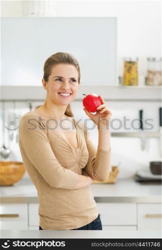 Portrait of thoughtful young housewife with apple in modern kitchen