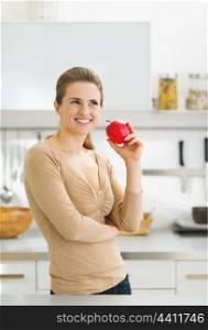 Portrait of thoughtful young housewife with apple in modern kitchen