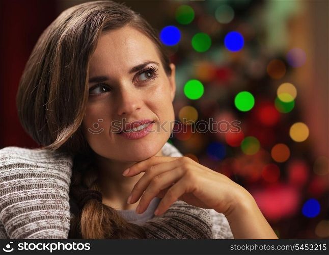 Portrait of thoughtful young woman near christmas tree looking on copy space