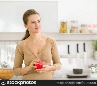 Portrait of thoughtful young woman with apple in modern kitchen