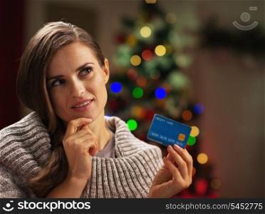 Portrait of thoughtful young woman with credit card near christmas tree