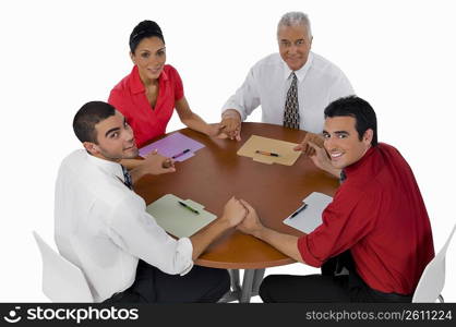 Portrait of three businessmen and a businesswoman sitting with holding their hands in a meeting
