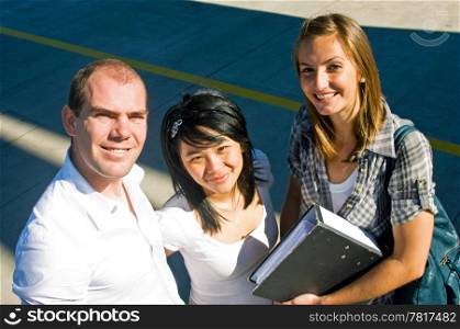 Portrait of three confidently smiling students on a shadowy concrete background