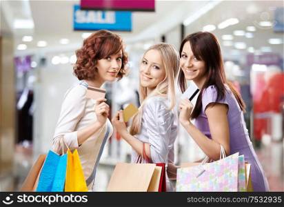 Portrait of three happy girls in shop, with three credit cards in hands
