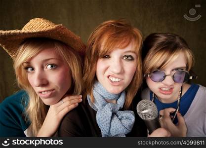 Portrait of three pretty young girls with a microphone making faces on green background