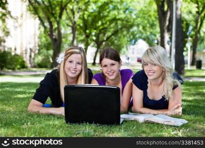 Portrait of three students working on laptop on campus ground