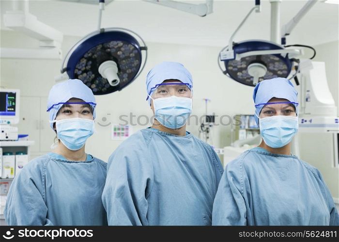 Portrait of three surgeons in a row wearing surgical masks in the operating room, looking at camera