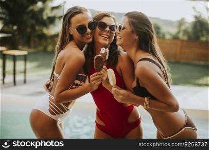 Portrait of three young attractive female friends eating ice cream by the swiiming pool on a summer day