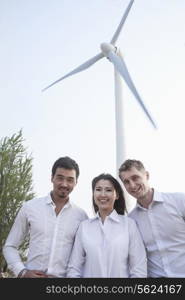 Portrait of three young business people standing in front of a wind turbine, looking at camera