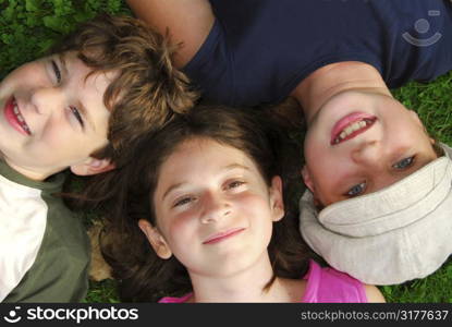 Portrait of three young children lying on grass looking up