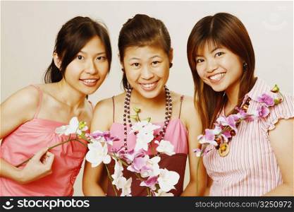 Portrait of three young women holding flowers and smiling
