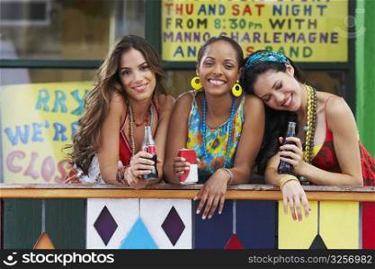 Portrait of three young women leaning on a railing and holding cold drinks