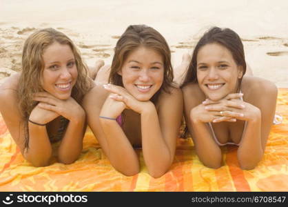 Portrait of three young women lying on a beach towel and smiling