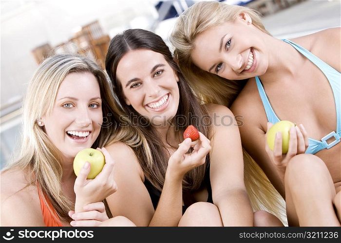 Portrait of three young women sitting holding fruit