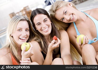 Portrait of three young women sitting holding fruit