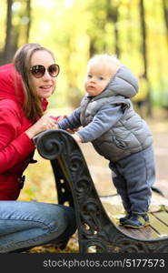 Portrait of toddler child in warm vest jacket outdoors. One year old baby boy in autumn park with his mother